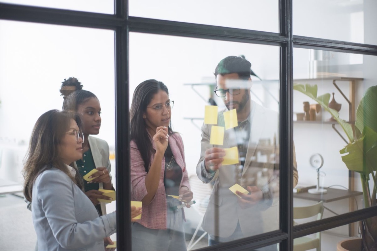 A team gathered around a glass wall, arranging sticky notes together